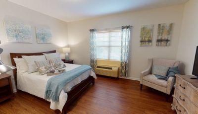 A well-lit bedroom with a bed, armchair, and window with curtains.