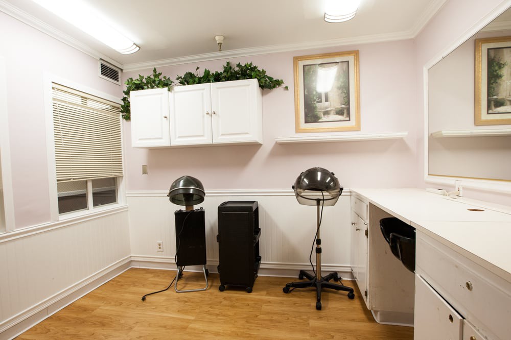 A neatly arranged salon interior featuring hair drying stations, white cabinets, and wooden flooring.
