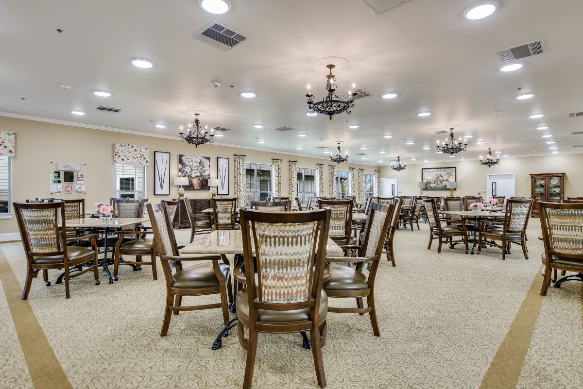 A spacious dining hall with neatly arranged tables and chairs under elegant chandeliers.