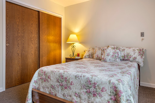 A cozy bedroom featuring a floral-patterned bedspread, a bedside lamp, and wooden closet doors.