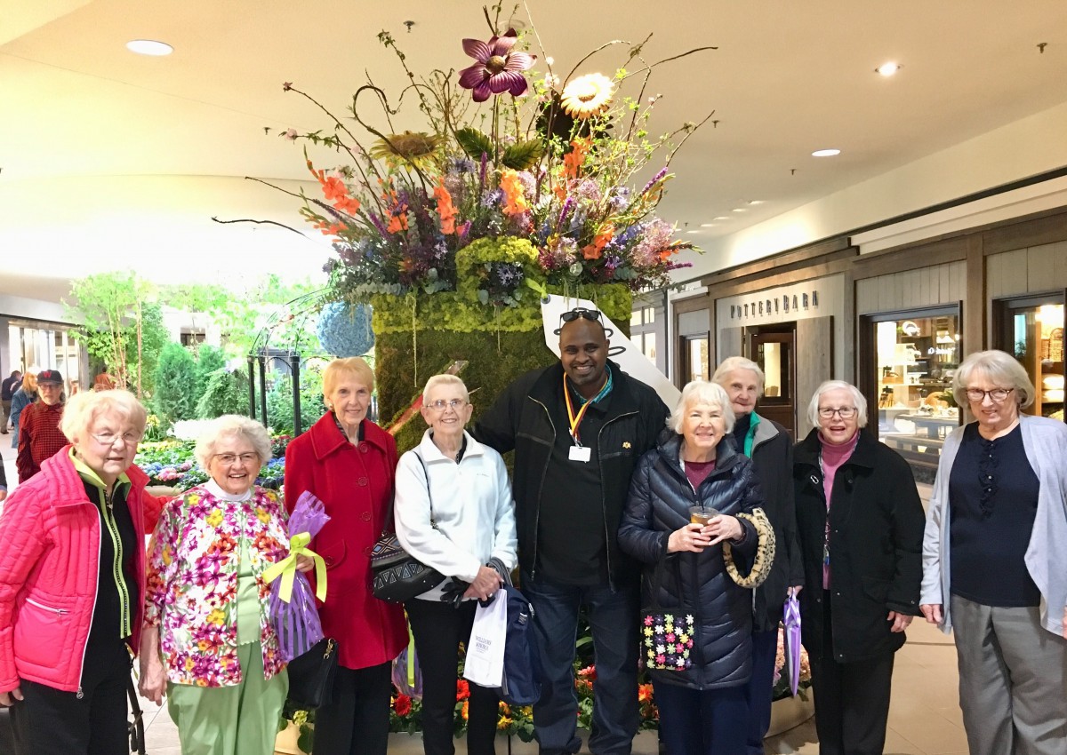A group of people posing in front of a large flower arrangement inside a mall.