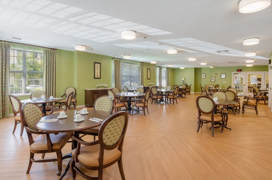 A spacious dining area with neatly arranged tables and chairs, featuring green walls and a wooden floor.