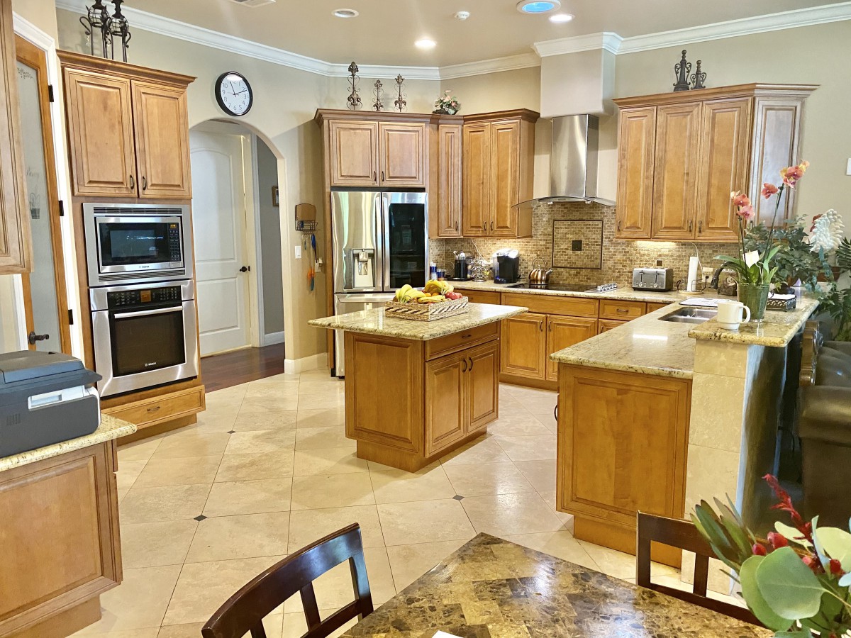 Spacious kitchen with wooden cabinets and a central island, featuring stainless steel appliances and a tile floor.
