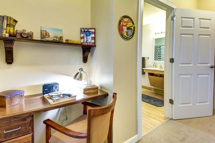 A small workspace with a desk, chair, and lamp next to an open door leading to a bathroom.