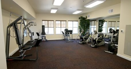 A well-lit gym with various exercise equipment and cardio machines.
