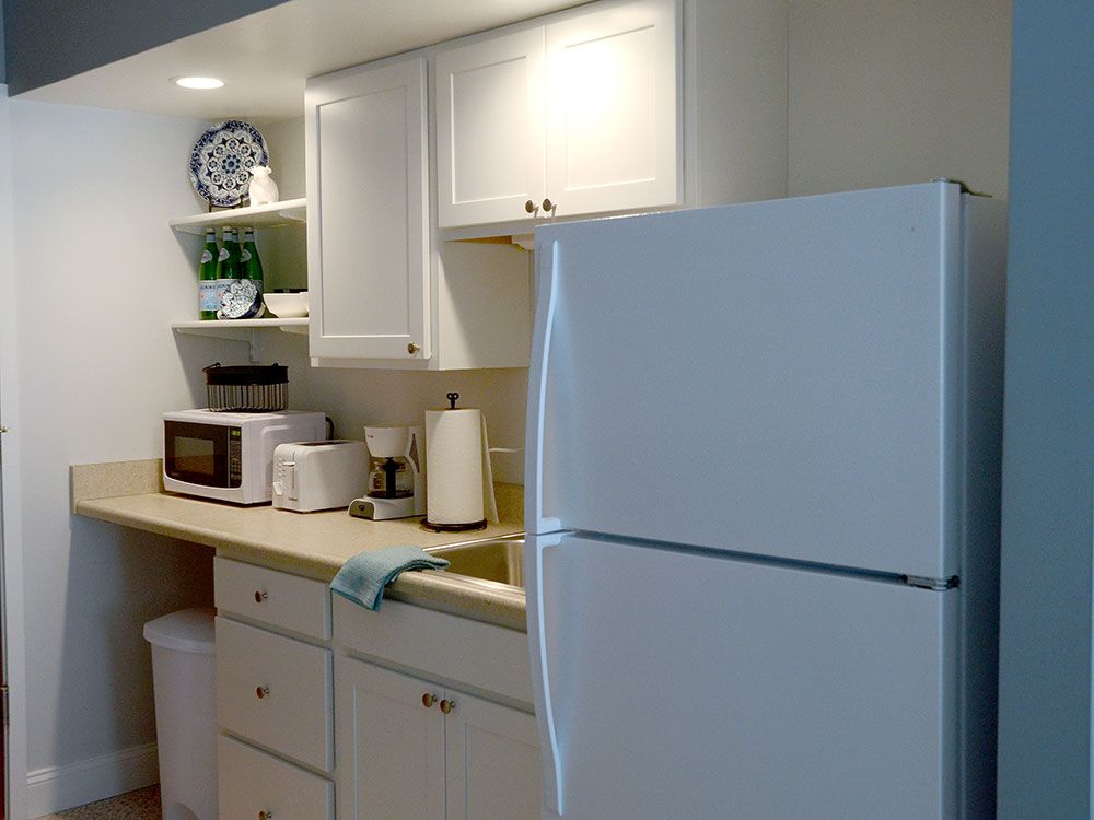 A tidy kitchen with white cabinets, featuring a refrigerator, microwave, and various kitchen appliances on the countertop.