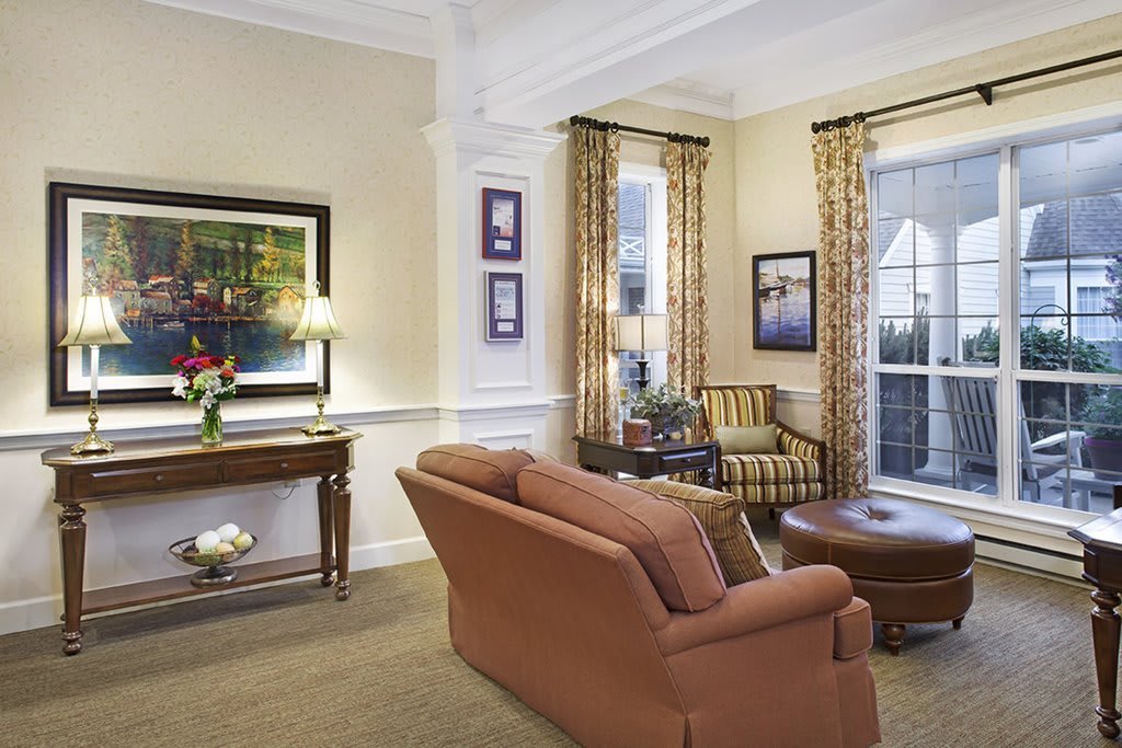 A well-furnished living room with a sofa, armchair, and coffee table decorated with artwork and curtains.