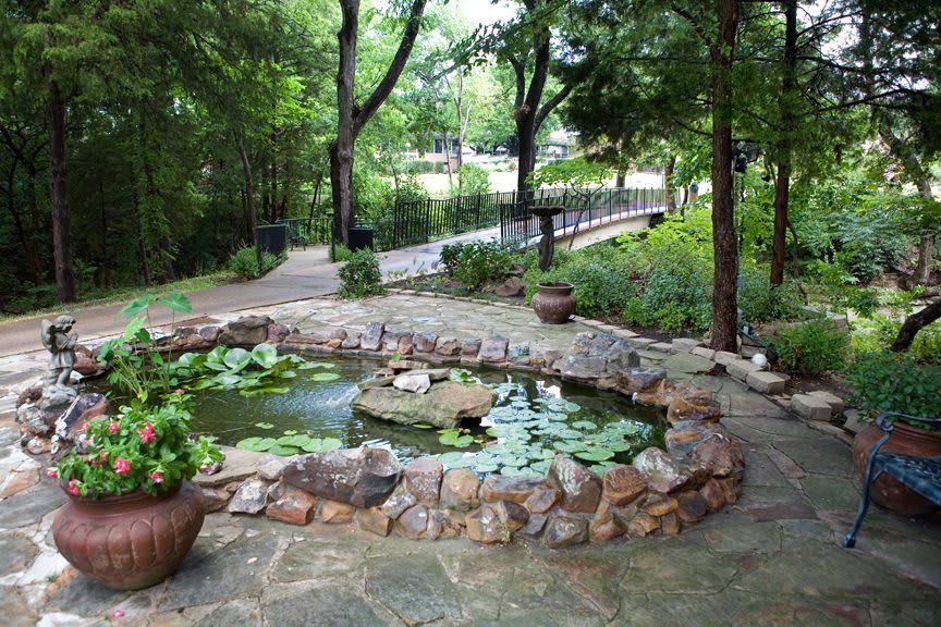 A peaceful garden pond surrounded by a stone path and lush greenery.