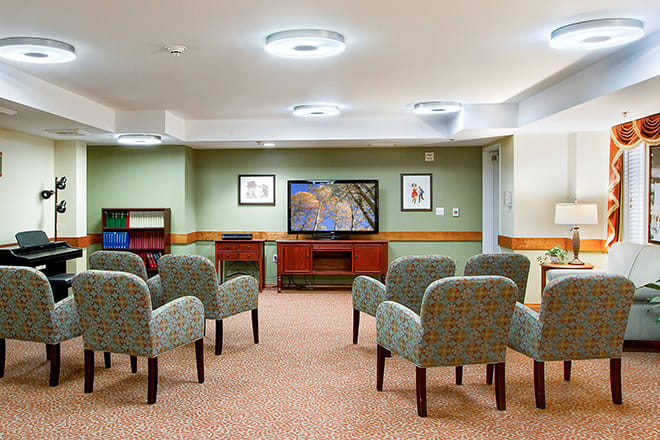 A waiting room with comfortable chairs facing a television and decorated with framed artwork.