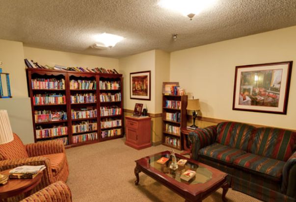 A cozy library room with bookshelves, comfortable seating, and warm lighting.
