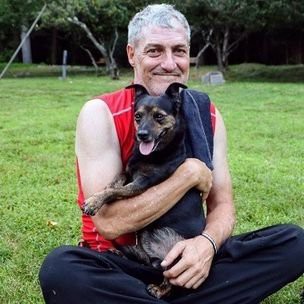 A man sitting in a park while holding and smiling with a dog.