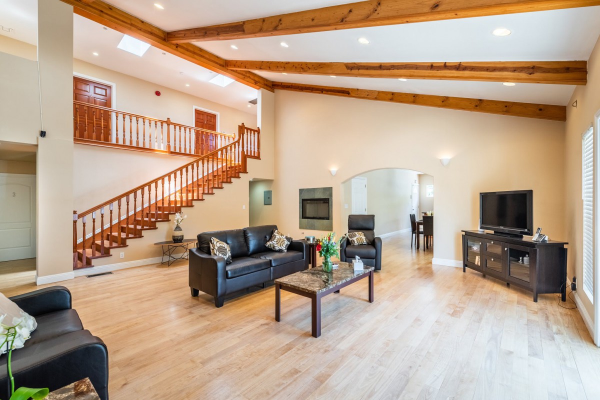 A modern, spacious living room with wood flooring, leather furniture, and exposed wooden beams.