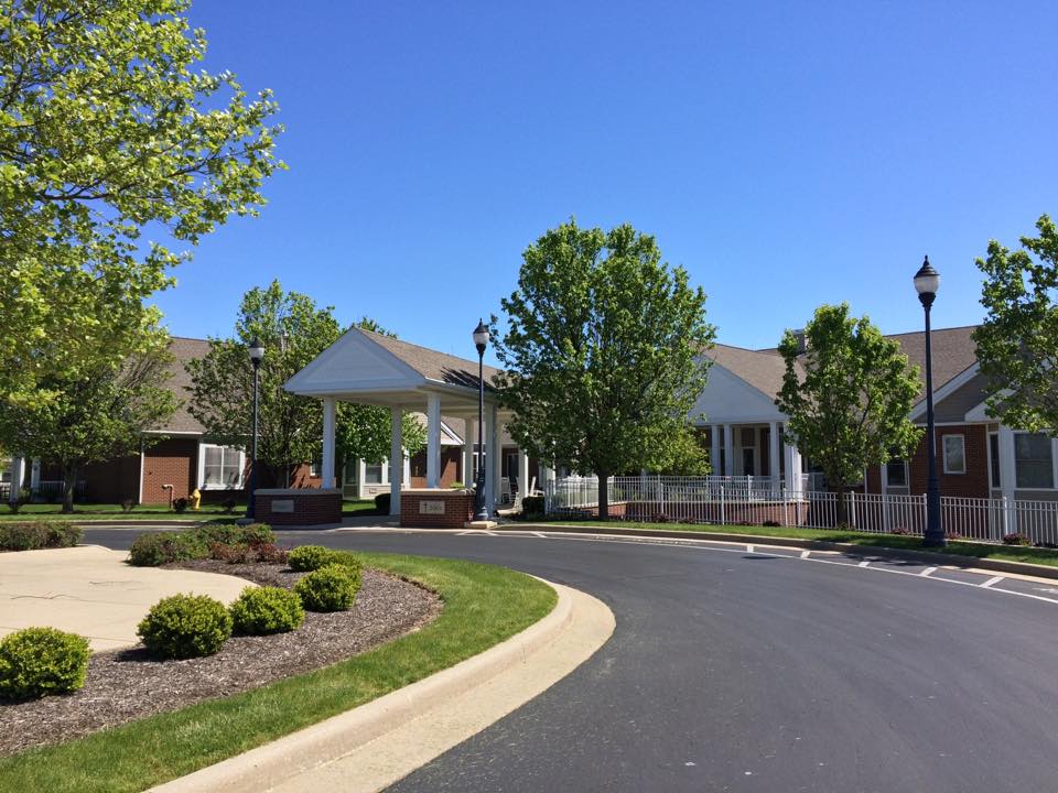 A suburban residential building with a driveway surrounded by trees and landscaping.