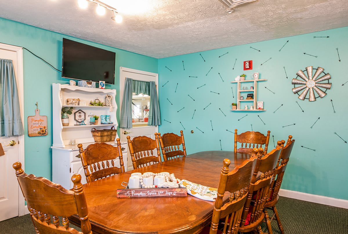 A cozy dining room with a wooden table and chairs, decorated with turquoise walls and a television.