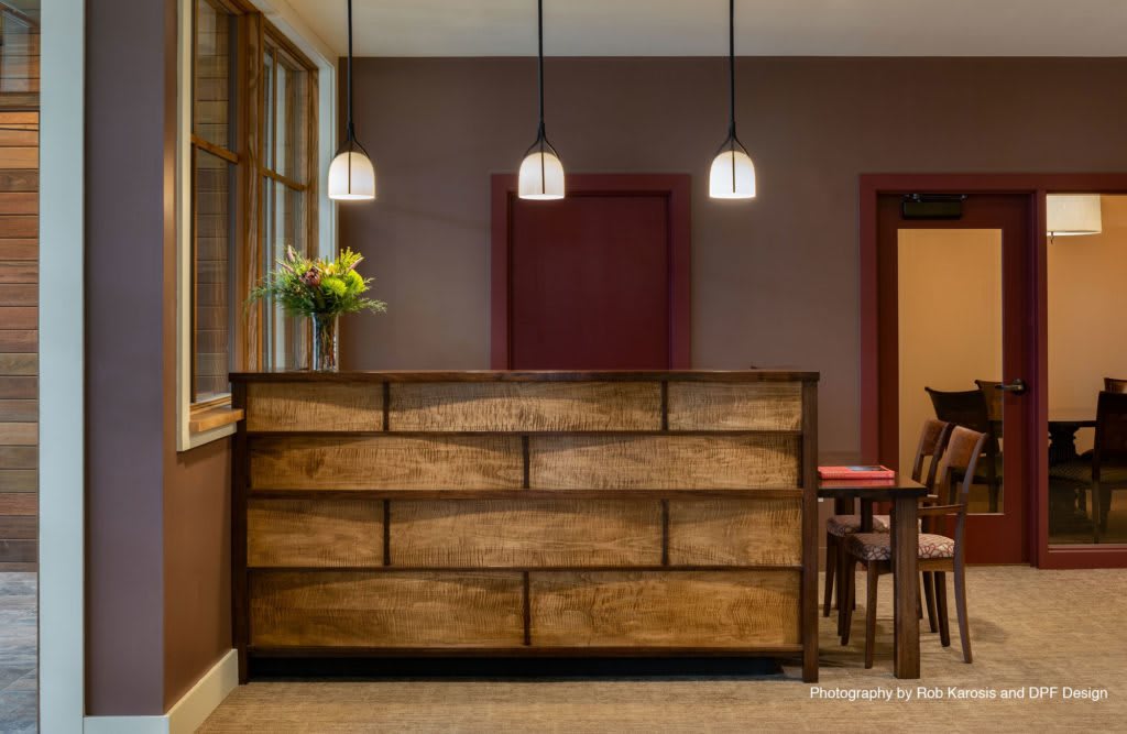 A cozy reception area with a wooden desk, pendant lights, and a vase of flowers.