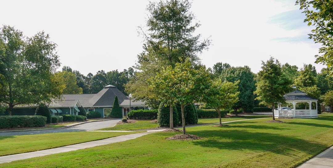 A suburban scene with a house, driveway, and trees on a grassy lawn.