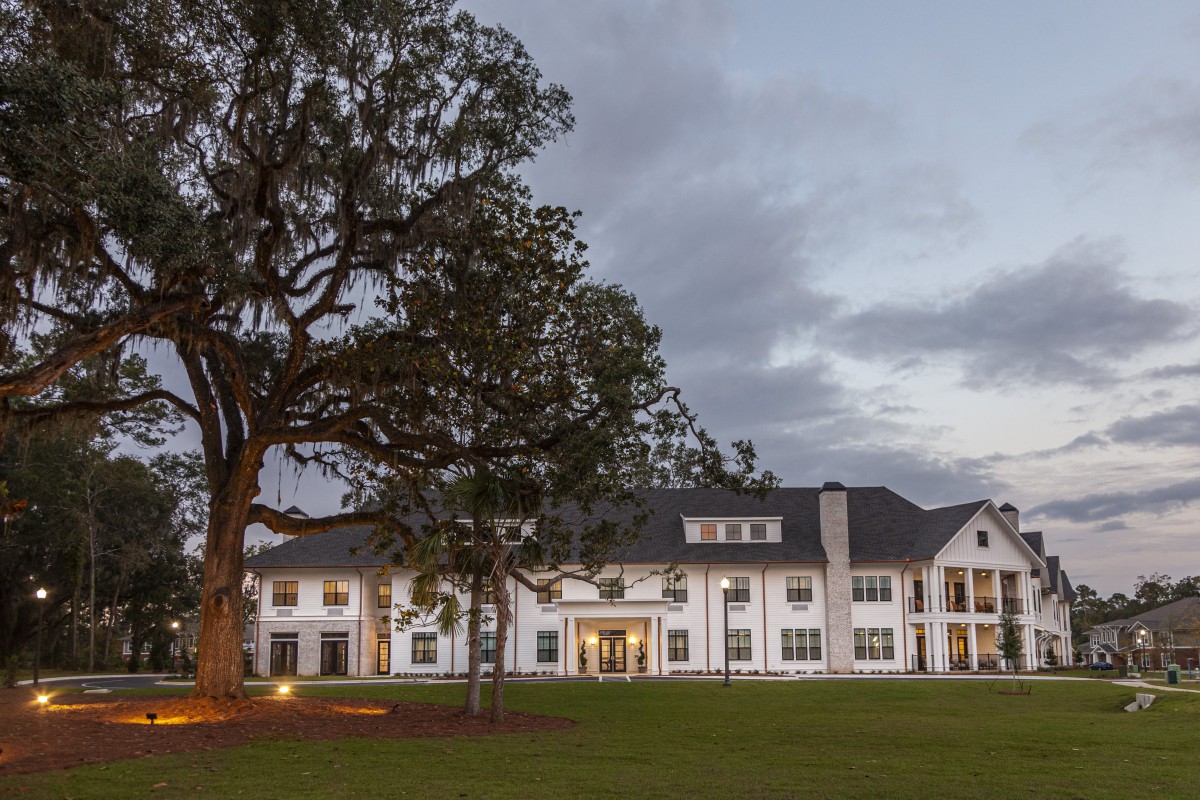 A large white residential house with a well-maintained lawn and a prominent tree at twilight.