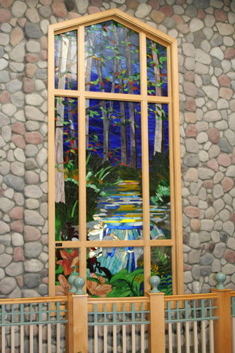 A beautifully crafted stained glass window depicting a serene forest scene with flowing water.
