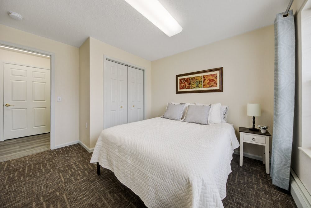 A neatly arranged bedroom with a bed, nightstand, lamp, and closet.