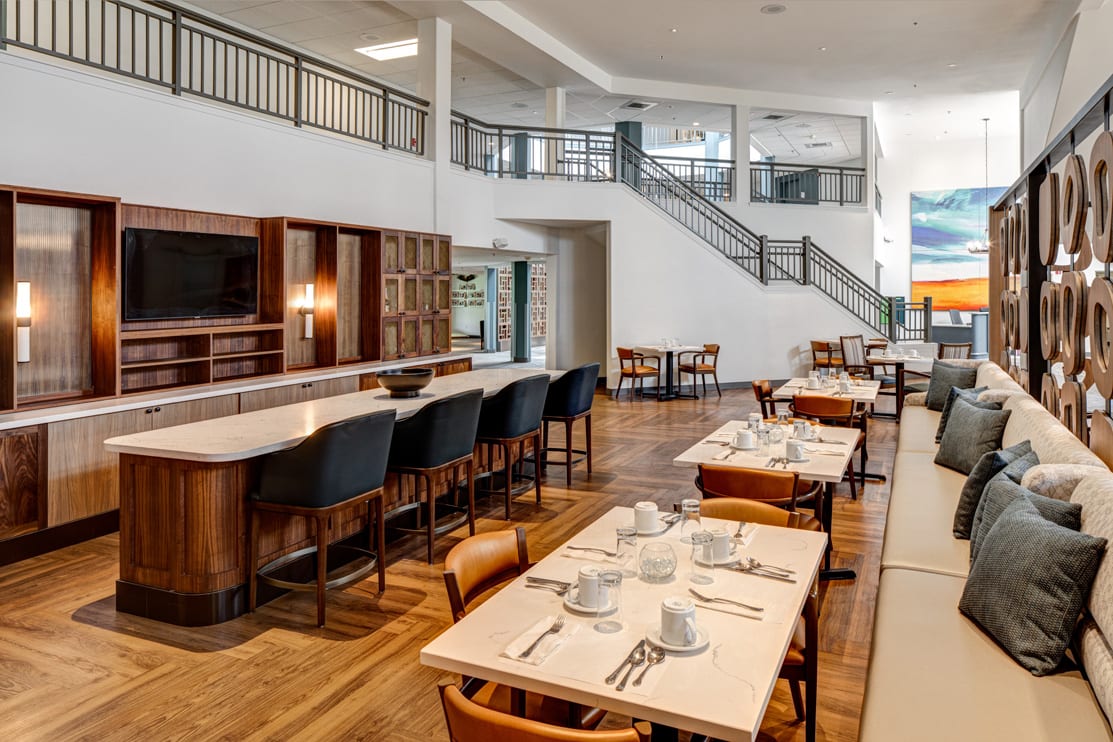 A modern restaurant interior with neatly arranged tables and chairs, featuring a counter seating area.