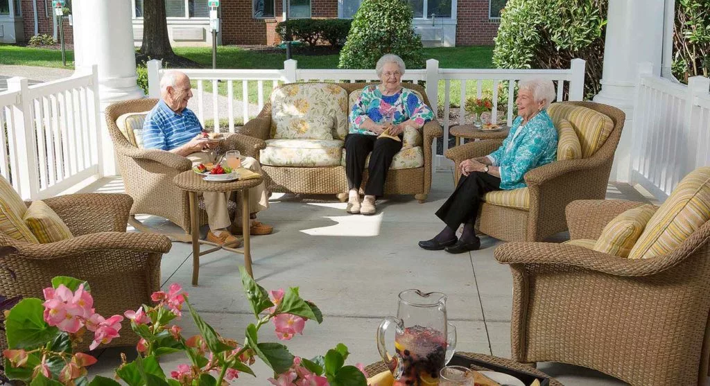 A group of elderly people socializing on a patio with comfortable furniture and plants.
