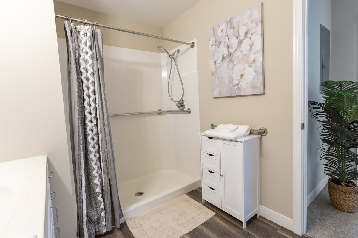 A modern bathroom with a shower, patterned curtain, and a small cabinet topped with towels.