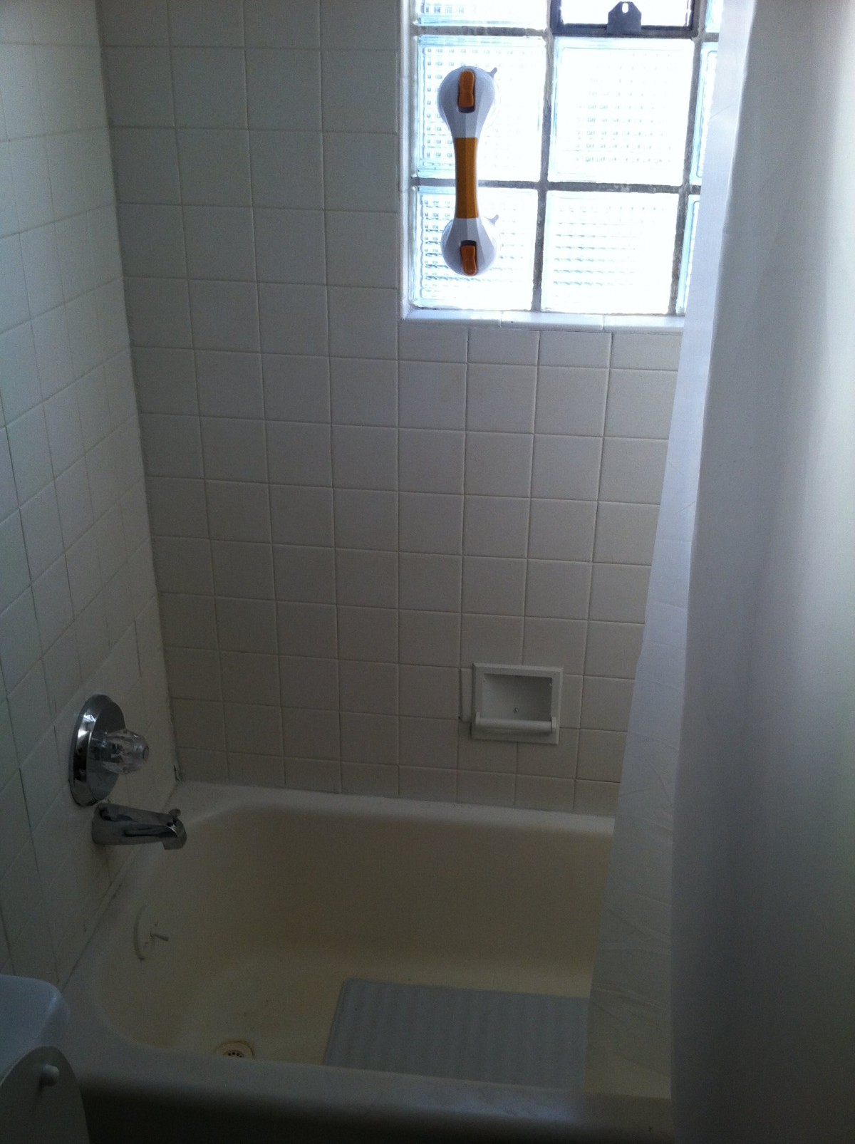 A small bathroom with a bathtub, tiled walls, and a window above the showerhead.