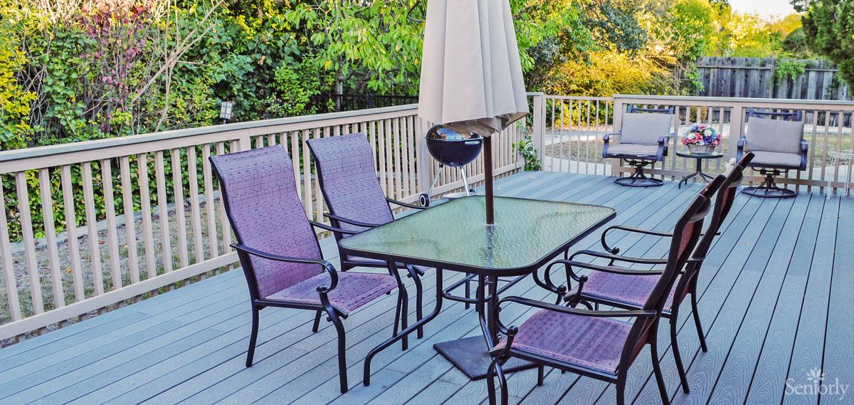 A tranquil patio setup with a glass table and chairs under an umbrella on a wooden deck.