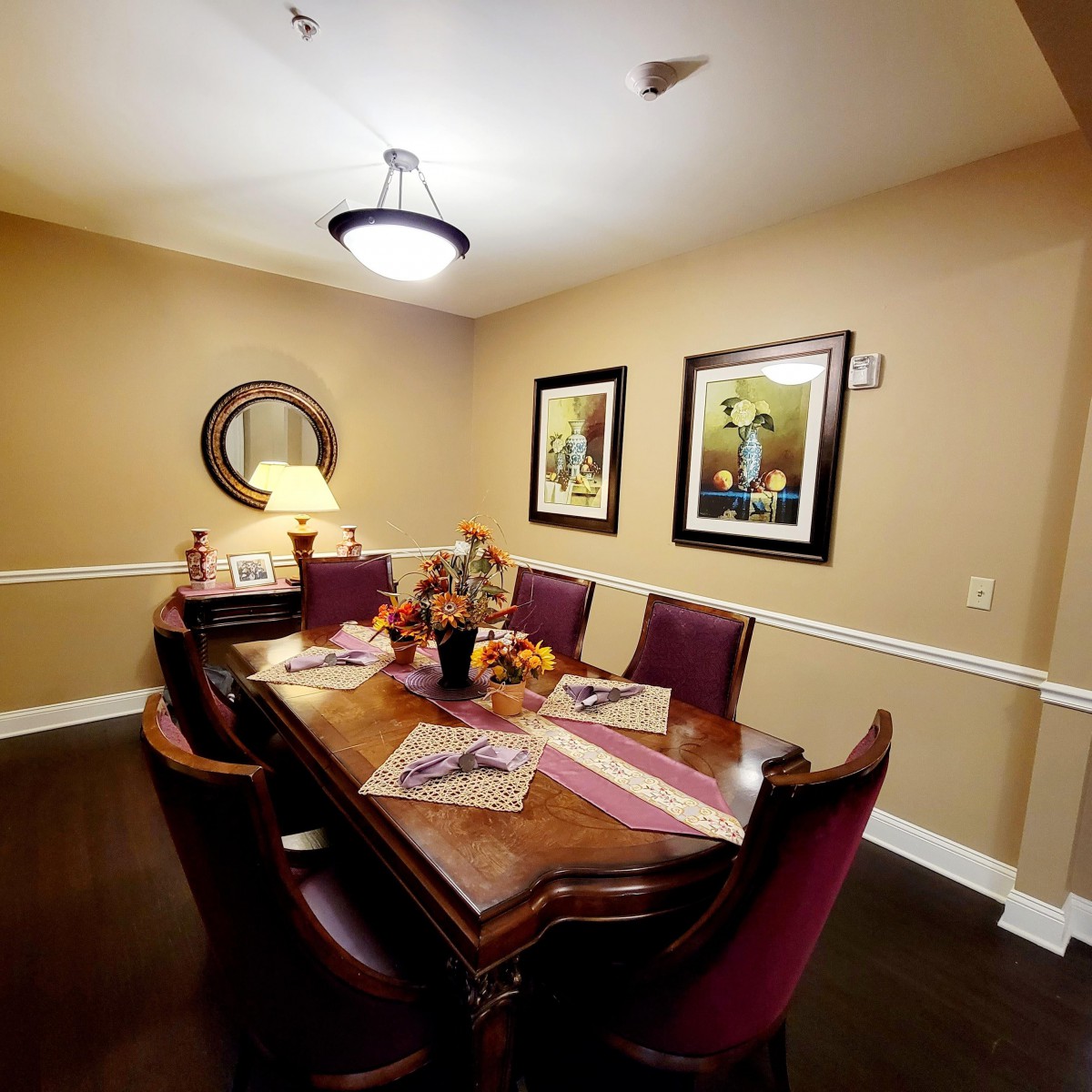 A warmly lit dining room featuring a wooden table with six chairs, adorned with decorative items and framed artwork on the walls.