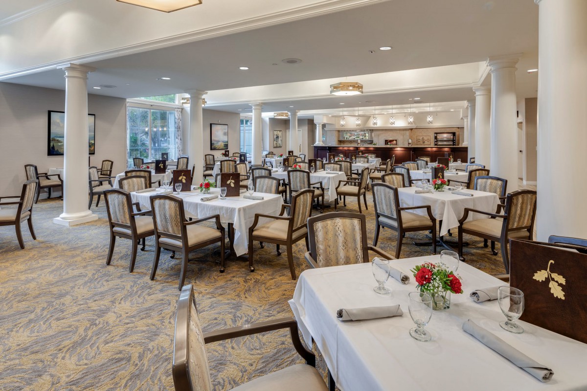 An elegant restaurant dining area with neatly arranged tables and chairs, featuring white tablecloths and floral centerpieces.