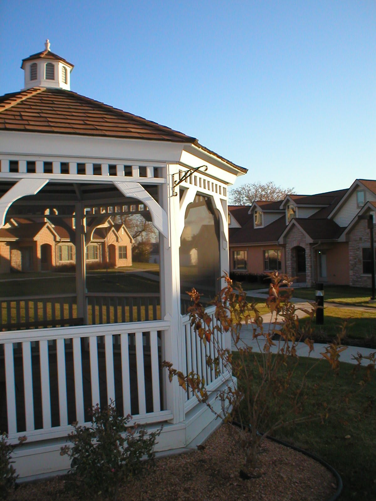 A gazebo in a garden setting with houses in the background on a sunny day.
