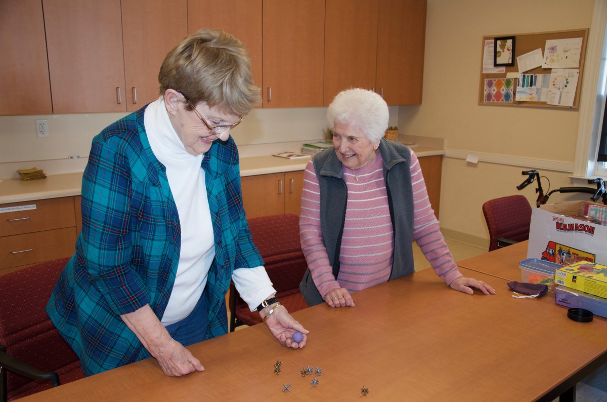 Two senior women enjoy a playful activity together indoors.