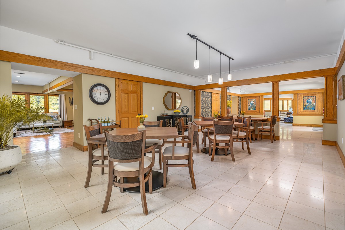 A spacious dining area featuring multiple tables and chairs, with stylish lighting and decorative elements such as a wall clock and mirror.