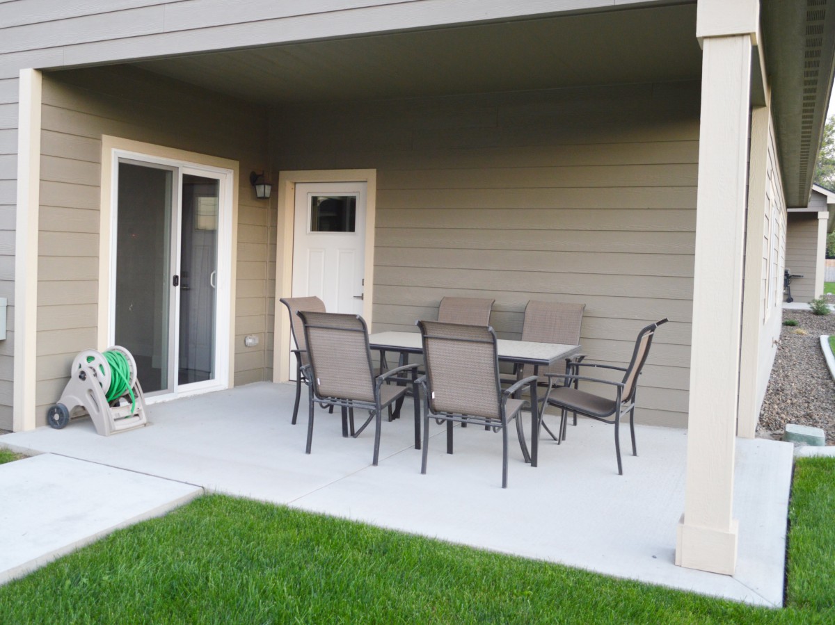 A covered patio area with outdoor furniture set in a backyard.