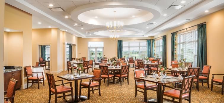 A well-furnished dining area with neatly arranged tables and chairs, elegant lighting fixtures, and large windows.