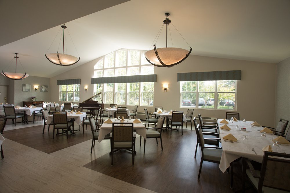 A spacious dining room with neatly arranged tables and chairs, featuring large windows and a grand piano.