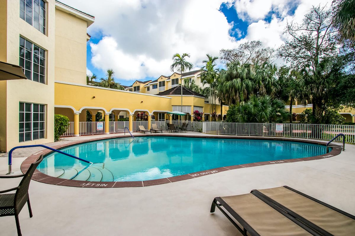 An inviting outdoor swimming pool surrounded by a scenic resort setting with palm trees under a bright, sunny sky.