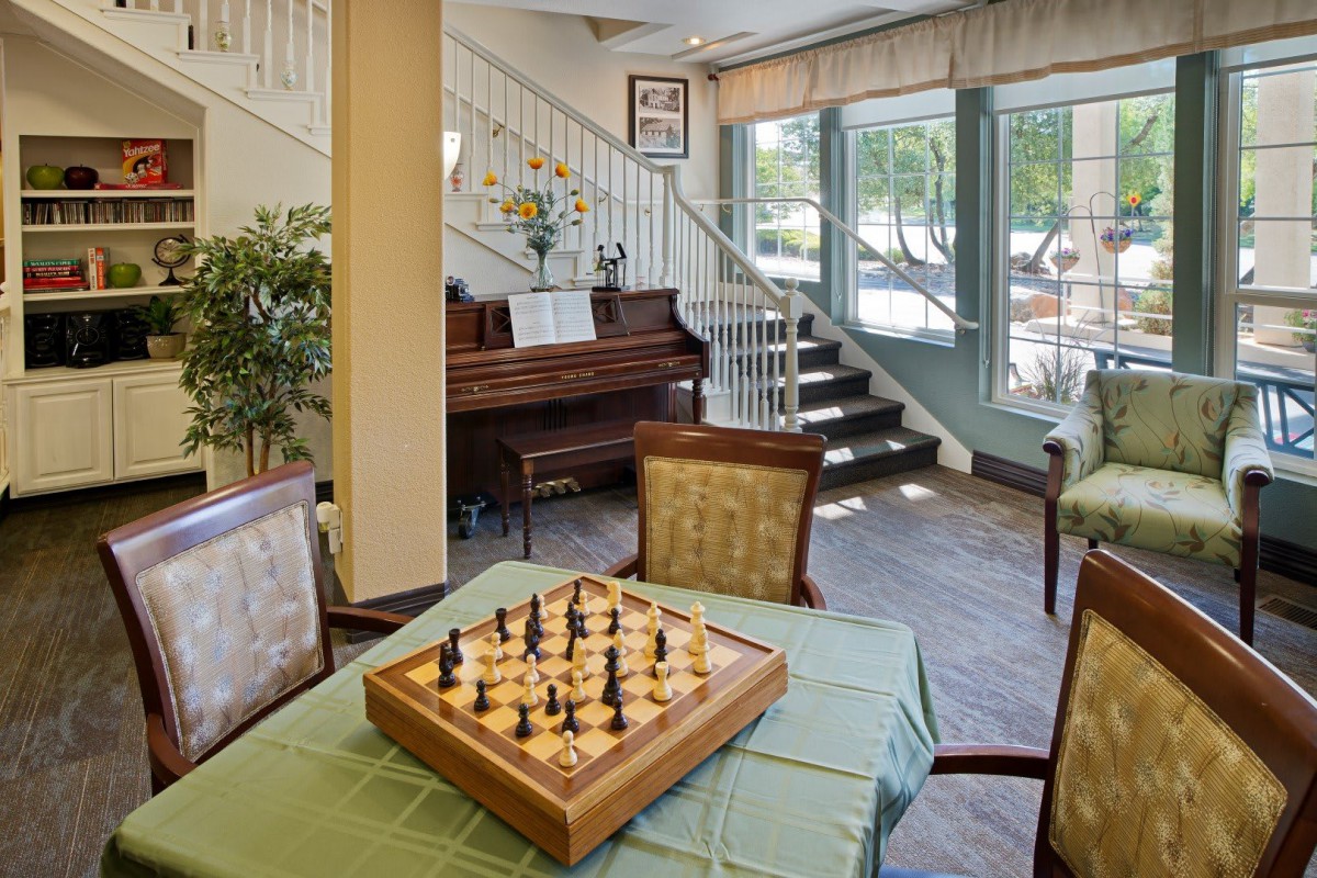 A cozy indoor setting featuring a chess board on a table, with a piano and stairway in the background.