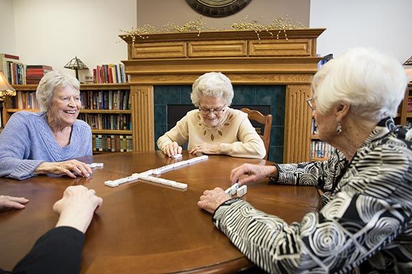 A group of elderly women engaged in a game of dominoes around a wooden table.