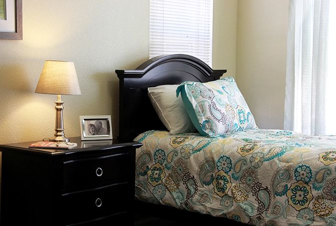 A cozy bedroom with a neatly made bed, nightstand, and lamp.