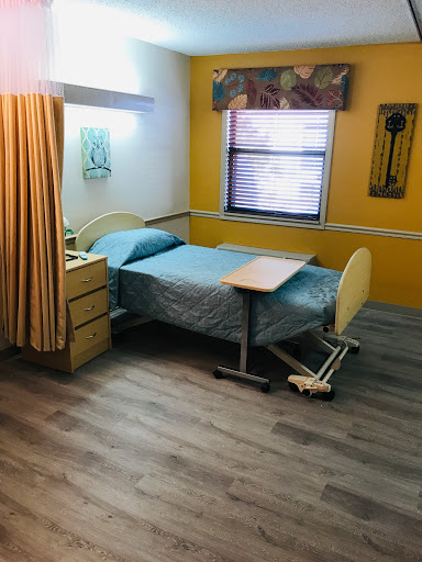 A cozy hospital room featuring a neatly made bed, wooden furniture, and warm yellow walls.