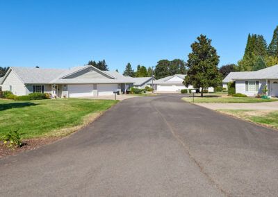 A quiet suburban neighborhood street lined with houses and trees under a clear blue sky.