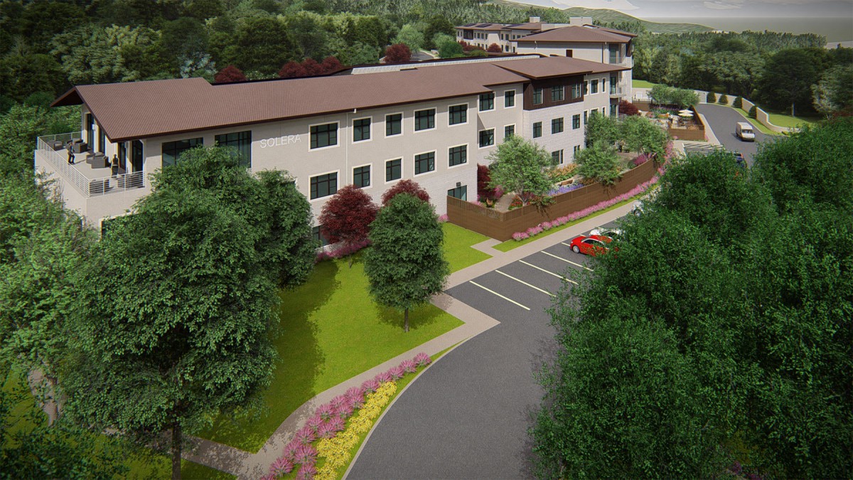 Aerial view of a modern building surrounded by greenery and a parking lot.