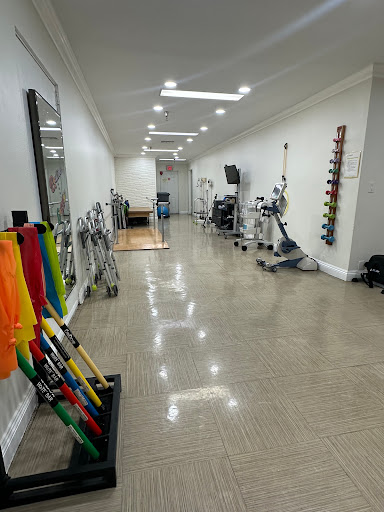 A well-lit gym space featuring various exercise equipment and rehabilitation tools along a spacious hallway.