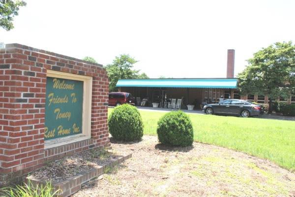 A restaurant with a brick sign and green awning, surrounded by neatly trimmed bushes.