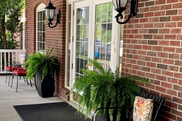 A cozy porch with potted plants and lanterns by a brick wall.
