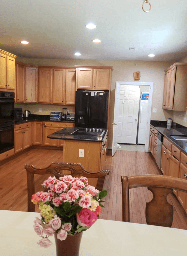 A spacious kitchen with wooden cabinets, black appliances, and a dining area featuring a vase of flowers.
