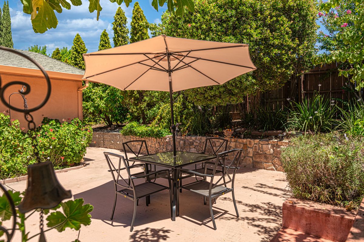 A sunny patio with outdoor furniture set, including a table, chairs, and an umbrella surrounded by lush greenery.