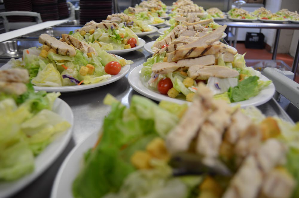 Plates of chicken salad arranged in a line, featuring lettuce, tomatoes, and vegetables.