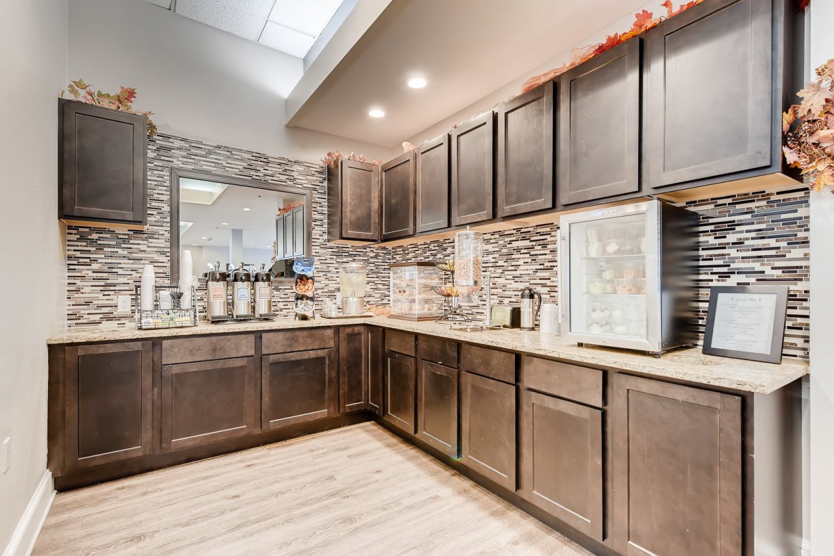 A modern kitchen interior featuring dark wooden cabinets, a well-equipped coffee station, and sleek countertops.